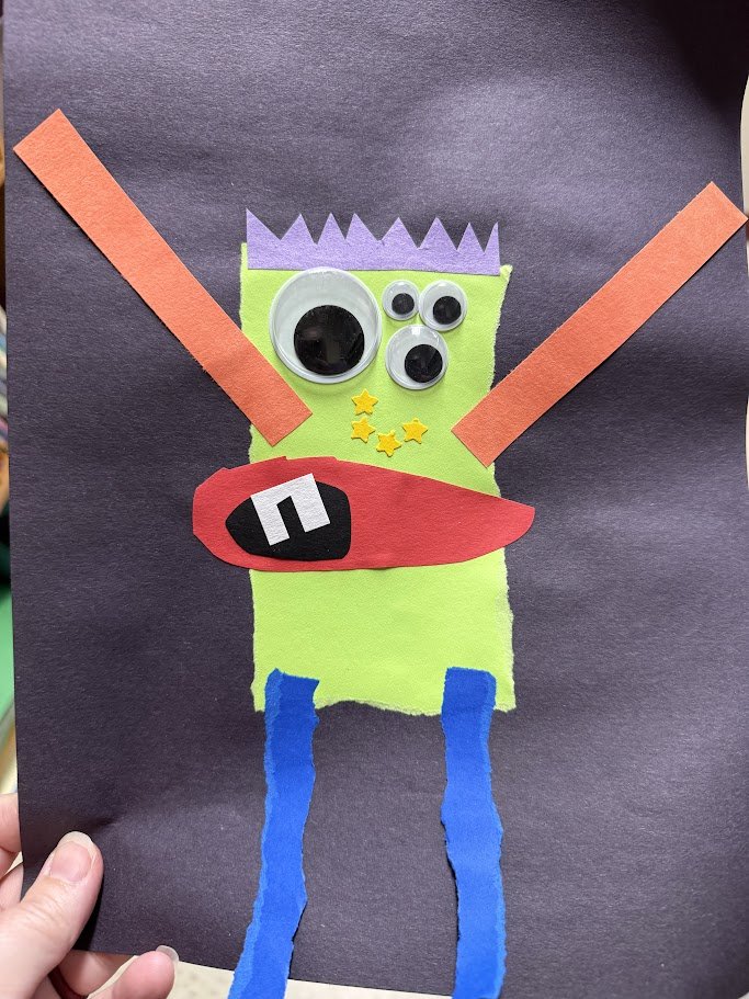 Paper monster craft: a lime green rectangle monster with a purple zigzag hairdo, three googly eyes, yellow star freckles, a red mouth with one tooth, orange arms raised and torn blue legs, on dark purple paper
